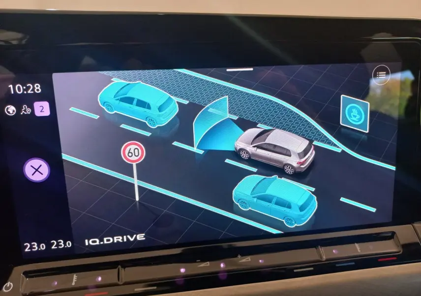 Affichage tactile intérieur montrant la Volkswagen Golf grise en vue 3D avec voitures bleues et panneau 60 km/h.