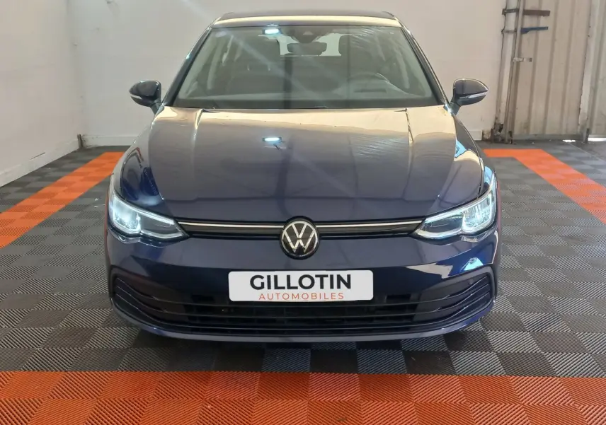 Vue frontale d'une Volkswagen Golf bleu nuit avec phares LED allumés dans un garage.