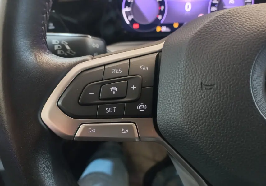 Gros plan sur les commandes du volant côté gauche d'une Volkswagen Golf bleue, tableau de bord numérique en arrière-plan.