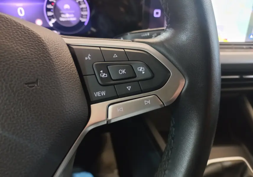 Gros plan sur les commandes du volant côté gauche en cuir noir de la Volkswagen Golf bleue 2022, tableau de bord numérique en arrière-plan.