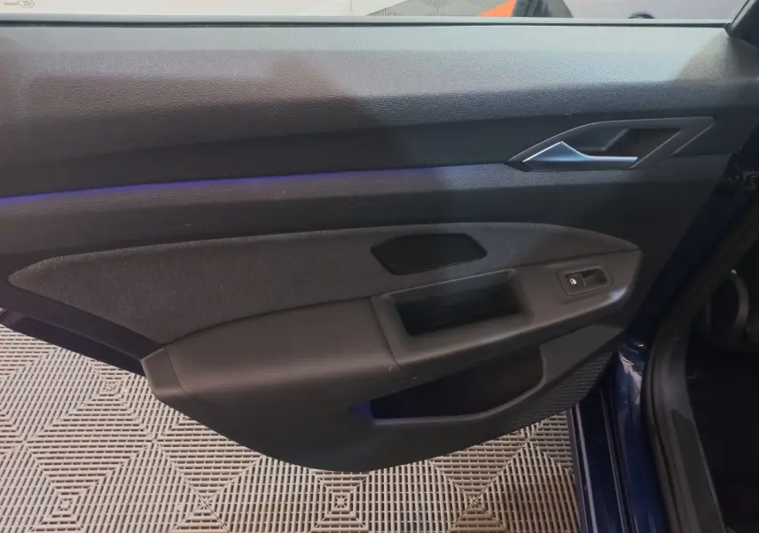 Vue rapprochée de la porte avant droite bleu foncé d'une Volkswagen Golf 2022 avec garniture noire et bouton de verrouillage électrique.