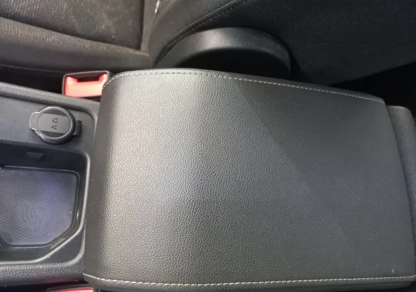 Gros plan sur l'accoudoir central noir en cuir avec prise 12V et compartiment de recharge sans fil dans une Volkswagen Golf bleue.