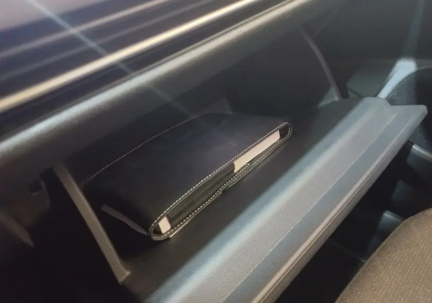 Gros plan sur la boîte à gants ouverte de la Volkswagen Golf 1.5 bleu, avec un carnet noir à l'intérieur.