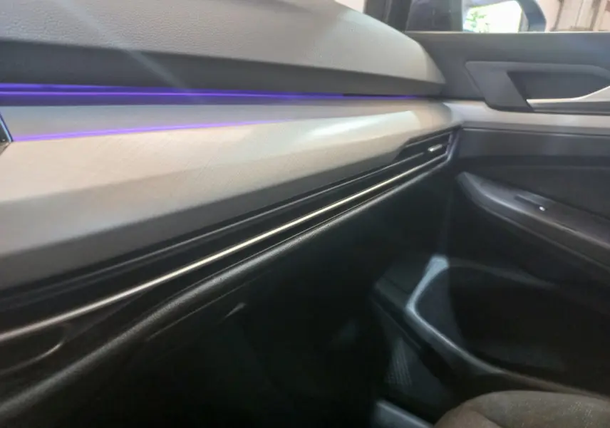 Détail intérieur côté passager de la Volkswagen Golf 2022, tableau de bord clair avec éclairage d'ambiance violet.