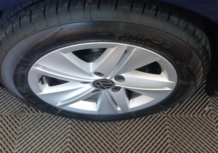 Gros plan sur la jante argentée avec logo Volkswagen, entourée du pneu noir sur carrosserie bleue.