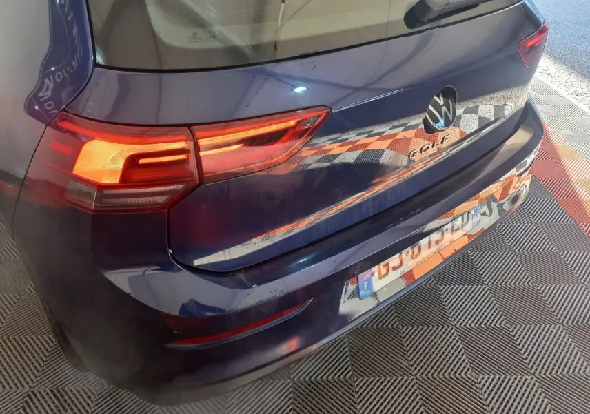 Vue 3/4 arrière droite d'une Volkswagen Golf bleue 2022 avec feux LED allumés et logo visible sur le hayon.
