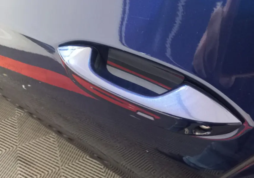 Poignée de porte bleue métallisée de Volkswagen Golf 2022, vue rapprochée côté gauche avec reflet rouge au sol.
