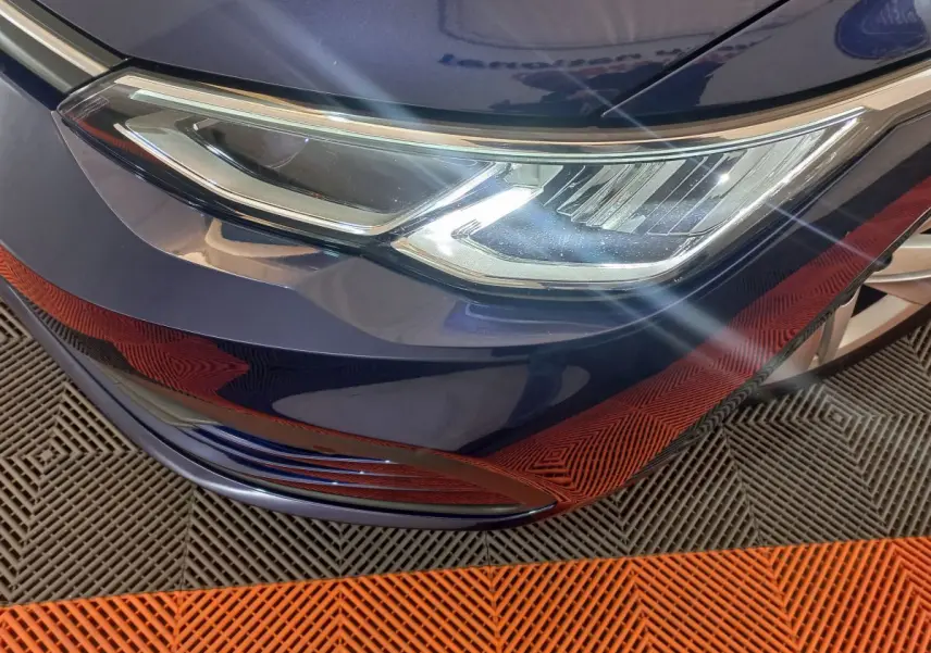 Gros plan sur le phare avant droit d'une Volkswagen Golf bleu 2022, avec reflets lumineux sur le capot.