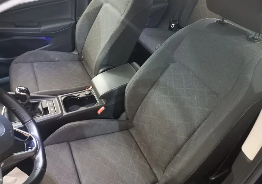 Intérieur avant de la Volkswagen Golf 2022, sièges tissu gris avec console centrale et volant cuir visible côté gauche.