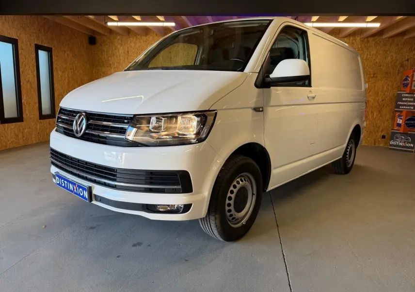 Vue 3/4 avant droit d’un Volkswagen Transporter blanc, fourgon utilitaire avec jantes tôles et calandre noire.