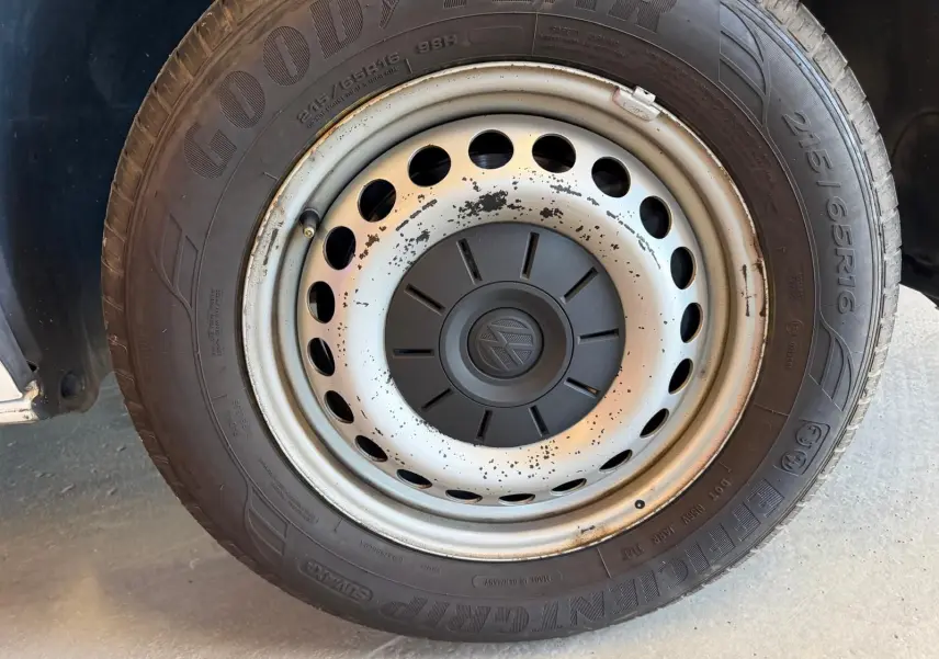 Gros plan sur la roue avant droite d’un Volkswagen Transporter blanc, jante acier avec logo VW au centre.