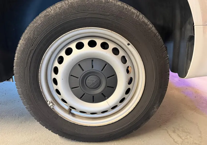Gros plan sur la roue avant droite du Volkswagen Transporter blanc, avec jante acier et logo VW au centre.