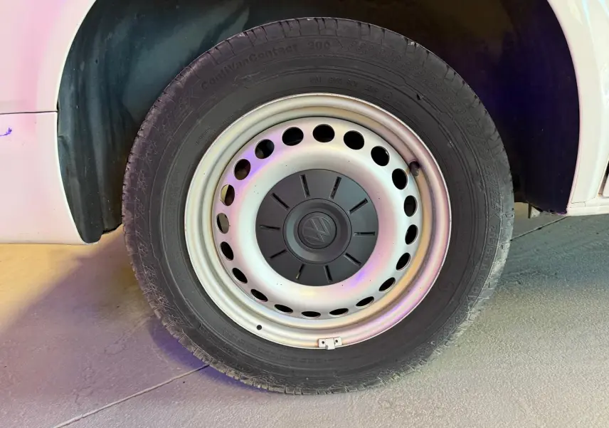 Gros plan sur la roue avant gauche du Volkswagen Transporter blanc, mettant en valeur la jante acier avec logo central.