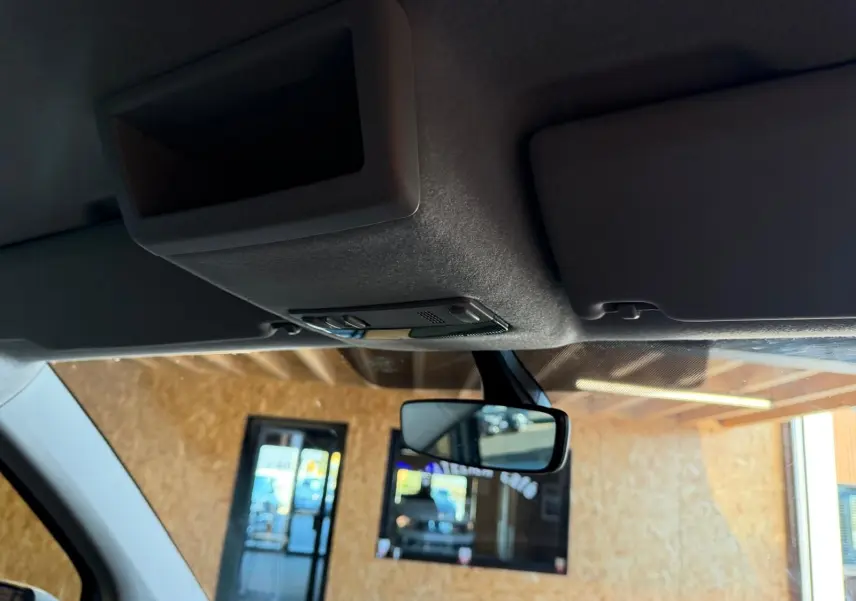 Vue intérieure du pare-soleil et du rétroviseur central du Volkswagen Transporter blanc, sous un abri en bois.