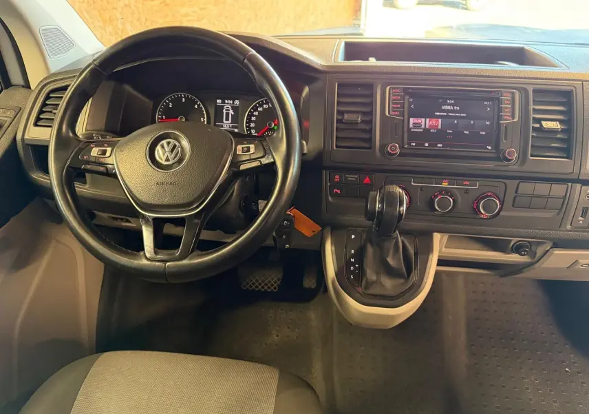 Vue intérieure du tableau de bord du Volkswagen Transporter blanc, avec volant, écran tactile et levier de vitesses automatique.