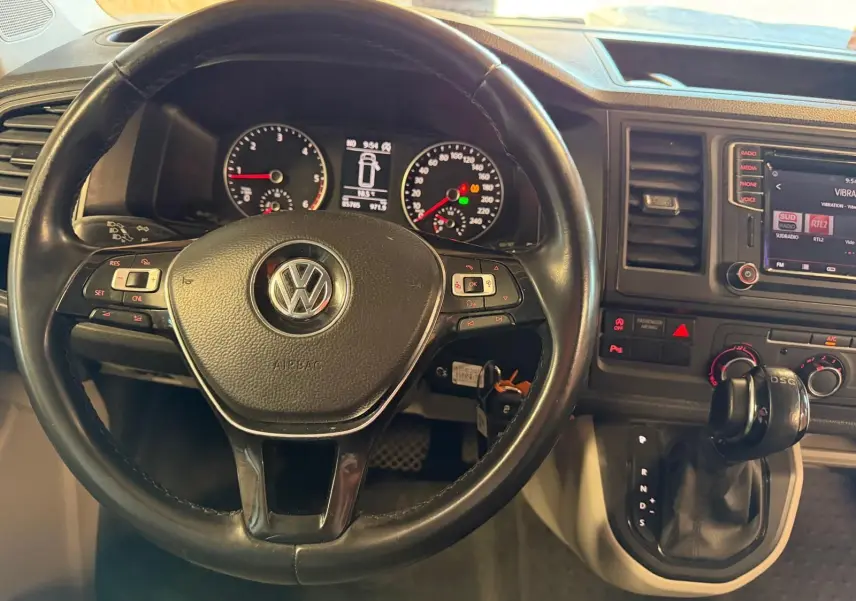 Vue rapprochée du volant noir et du tableau de bord du Volkswagen Transporter blanc, avec levier de vitesse DSG visible.