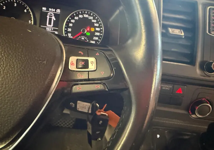 Vue rapprochée du volant noir et du tableau de bord du Volkswagen Transporter blanc, avec clés en contacteur et commandes au volant.