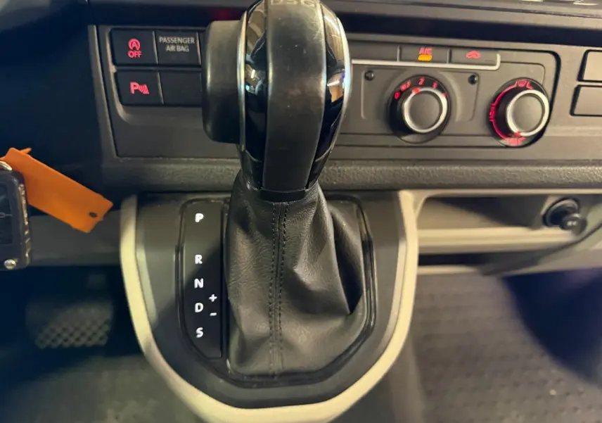 Gros plan sur le levier de vitesse automatique DSG noir du Volkswagen Transporter blanc, avec commandes de climatisation en arrière-plan.