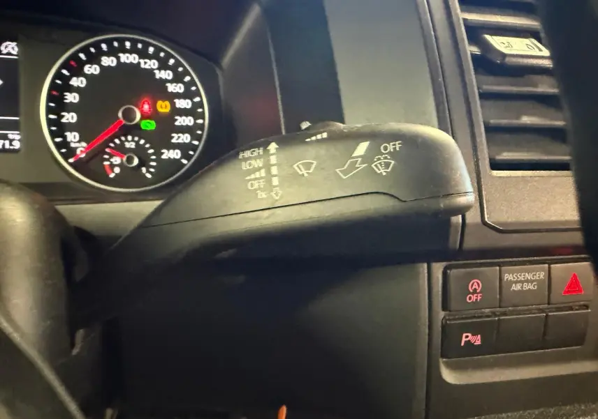 Gros plan sur la commande d’essuie-glace du Volkswagen Transporter blanc, avec tableau de bord et voyants visibles en arrière-plan.
