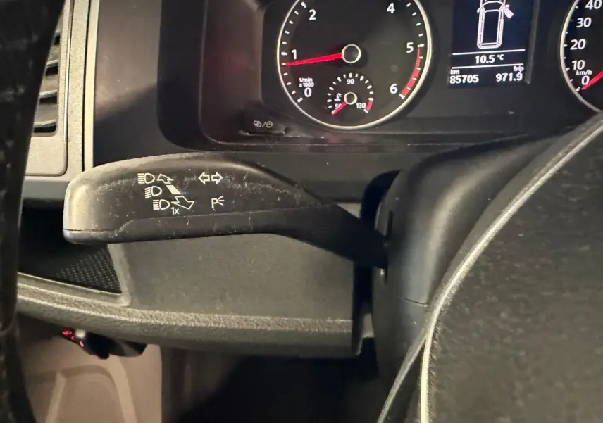 Gros plan sur le commodo de clignotant noir à gauche du volant, avec tableau de bord et compteurs du Volkswagen Transporter blanc.