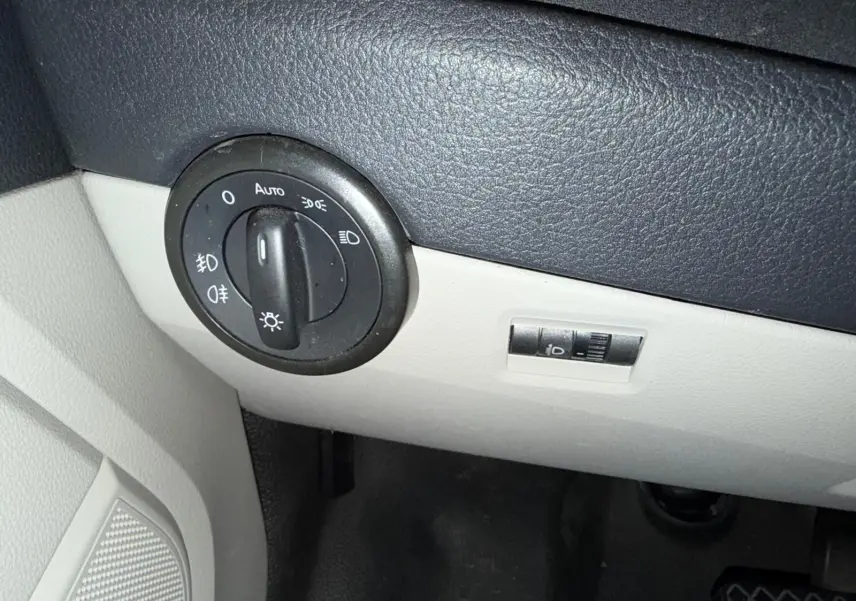 Gros plan sur le bouton de commande des phares dans l'habitacle gris et noir du Volkswagen Transporter blanc.