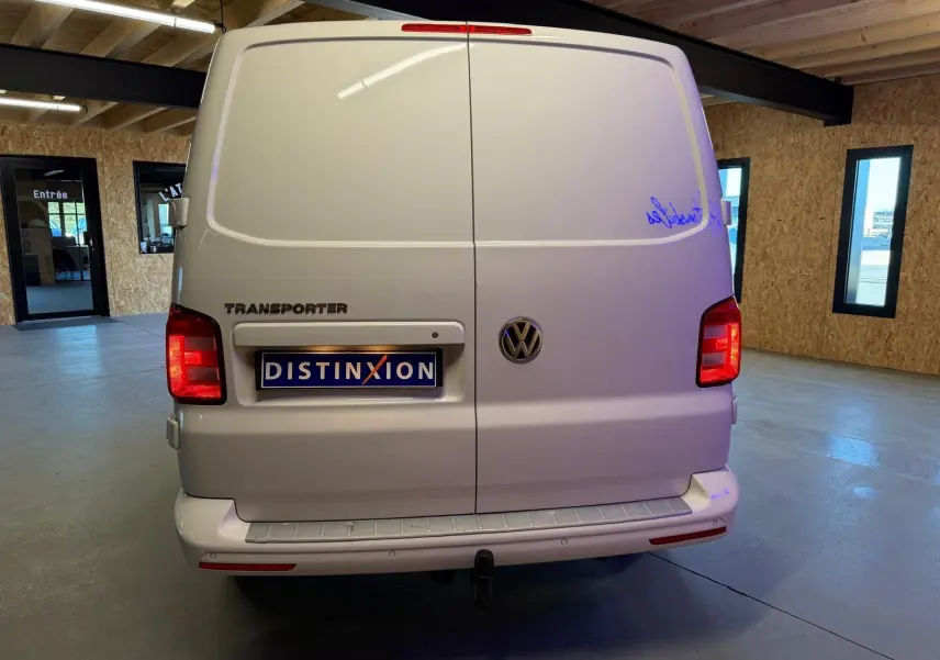 Vue arrière d'un Volkswagen Transporter blanc 2019 avec portes battantes et plaque Distinxion visible en intérieur.
