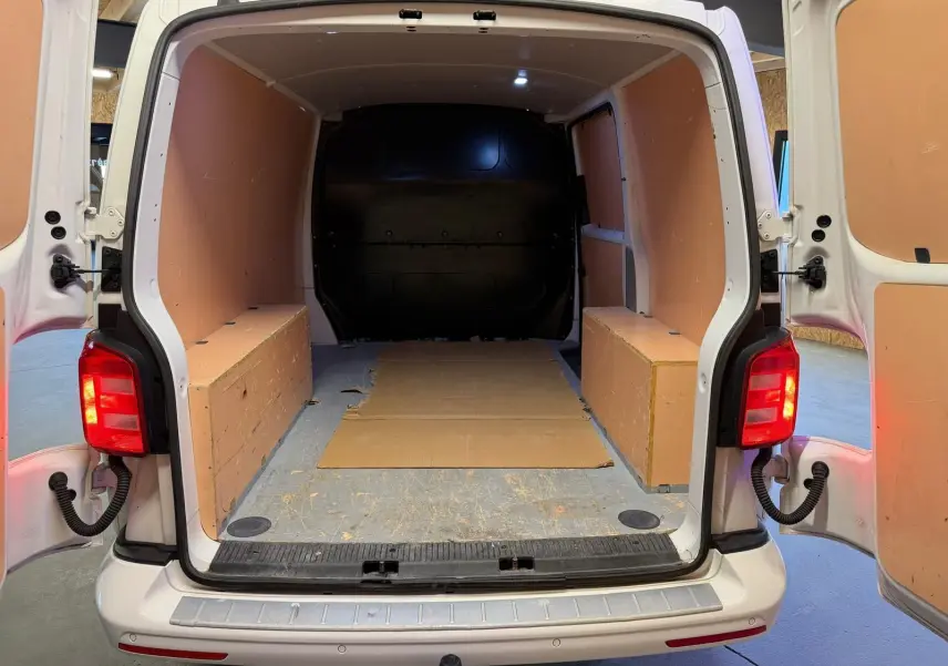 Vue arrière ouverte du Volkswagen Transporter blanc 2019, montrant l’espace de chargement vide avec panneaux latéraux en bois.