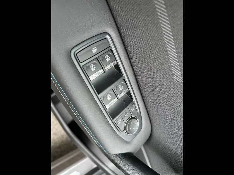 Gros plan sur les commandes des vitres électriques côté gauche du Renault Captur 2026, avec surpiqûres bleues et tissu noir.