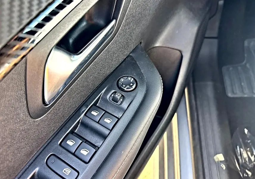 Gros plan sur la commande des vitres côté conducteur de la Peugeot 208 1.2 100 allure gris artense, intérieur noir.