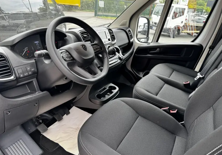 Intérieur avant droit du Peugeot Boxer Fourgon 2026, volant multifonctions, sièges gris et tableau de bord moderne.