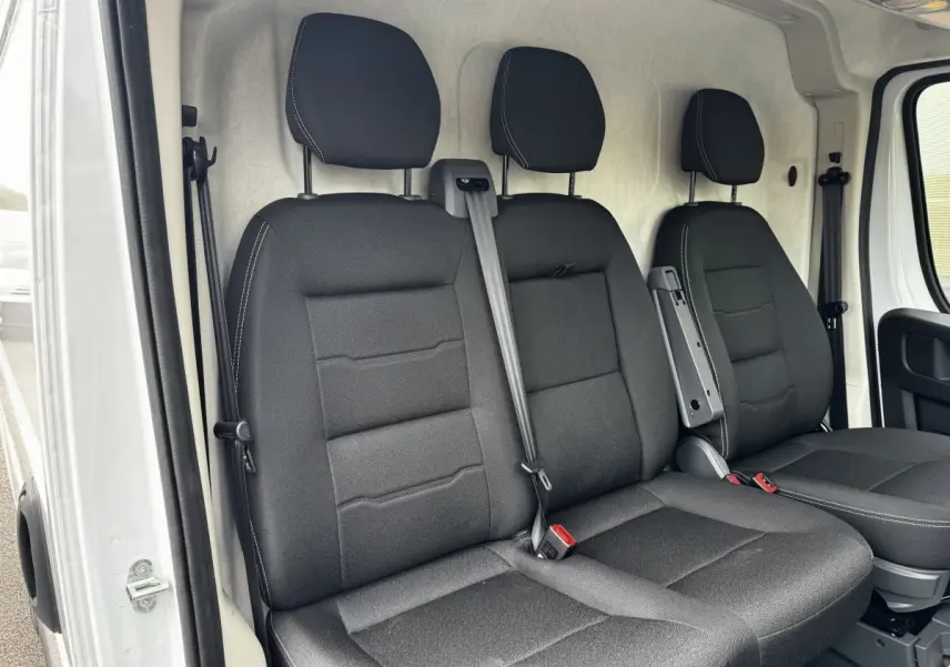 Vue intérieure des sièges avant noirs du Peugeot Boxer Fourgon blanc, avec ceinture de sécurité et accoudoir central.