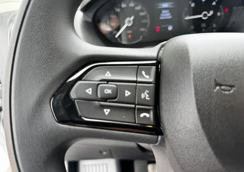Gros plan sur le volant multifonctions noir du Peugeot Boxer Fourgon, avec commandes de téléphone et navigation.