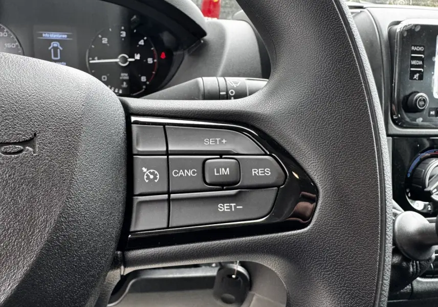 Gros plan sur les commandes du volant multifonctions noir du Peugeot Boxer Fourgon blanc, avec tableau de bord et écran tactile en arrière-plan.