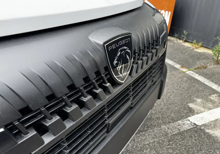 Gros plan sur la calandre noire et le logo Peugeot du fourgon blanc Peugeot Boxer L2H2 Diesel 2026.