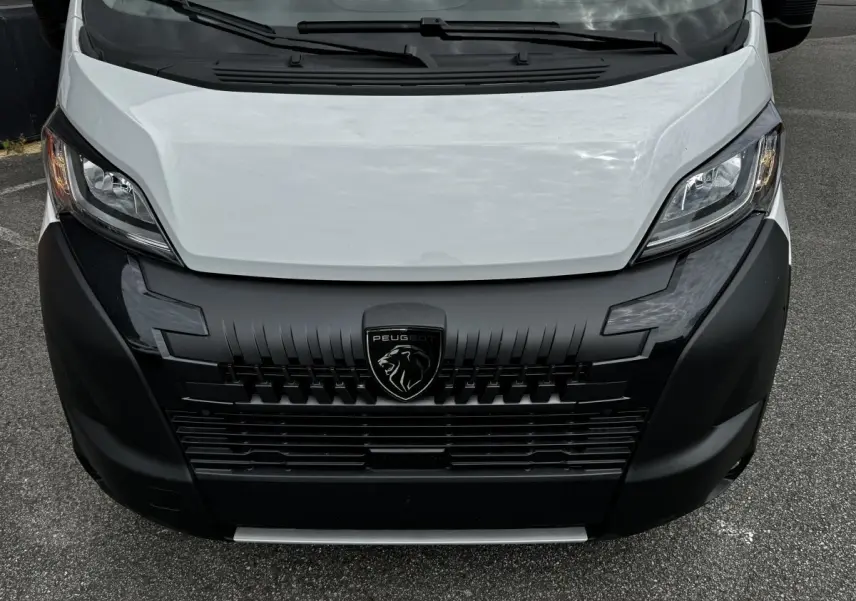 Vue avant rapprochée du Peugeot Boxer Fourgon blanc avec calandre noire et logo lion central bien visible.