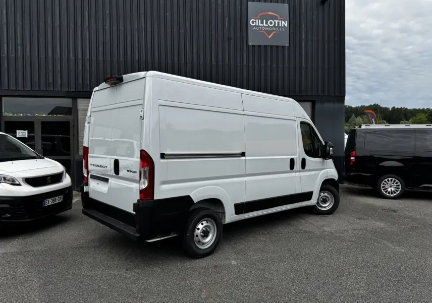Vue 3/4 arrière droite d’un Peugeot Boxer Fourgon blanc stationné devant un bâtiment commercial.