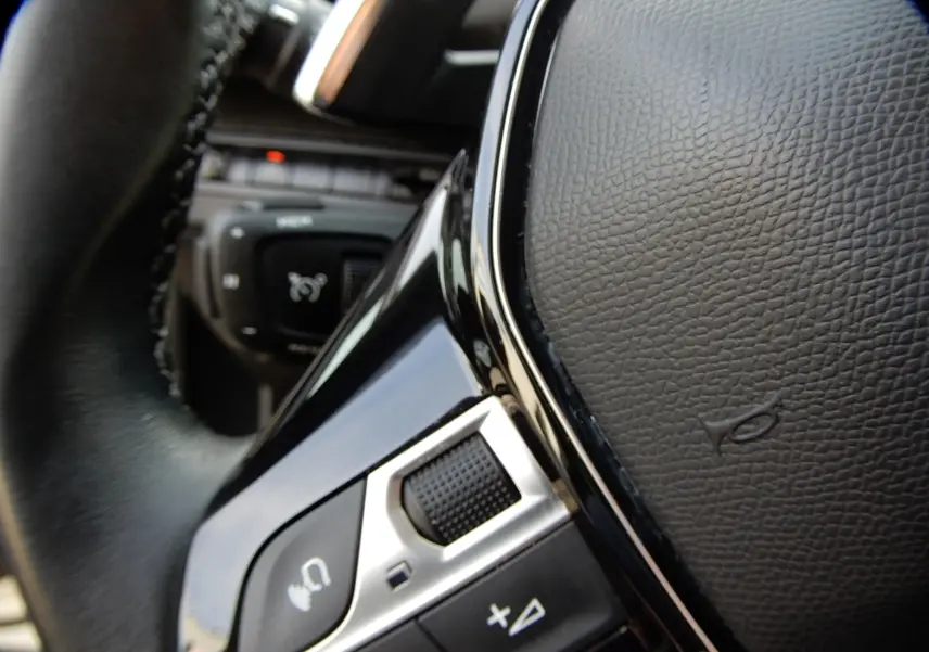 Gros plan sur la commande vocale et les boutons de volume du volant en cuir noir du Peugeot 5008 blanc nacré.