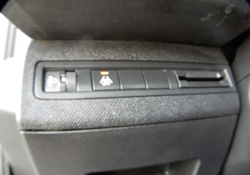 Gros plan sur les commandes noires du tableau de bord du Peugeot 5008 blanc nacré, avec un témoin orange allumé.