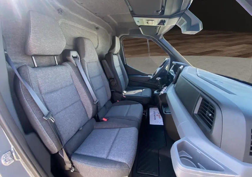 Vue intérieure côté passager du Renault Master 2025, sièges tissu gris chiné avec surpiqûres bleues et tableau de bord gris.