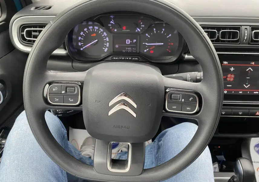 Vue rapprochée du volant multifonction noir de la Citroën C3 2023 avec tableau de bord et écran tactile en arrière-plan.