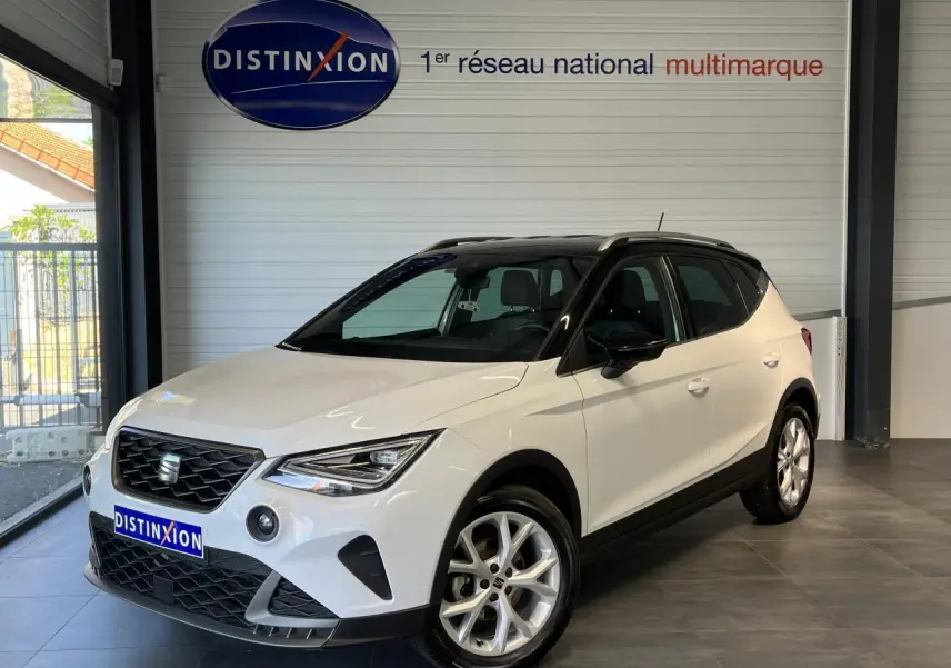 SEAT Arona blanc Nevada vue 3/4 avant en intérieur, toit noir et jantes alliage 16 pouces design.