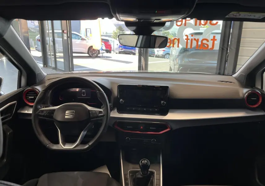 Vue intérieure frontale du tableau de bord du SEAT Arona blanc Nevada 2024 avec volant sport cuir et écran tactile central.