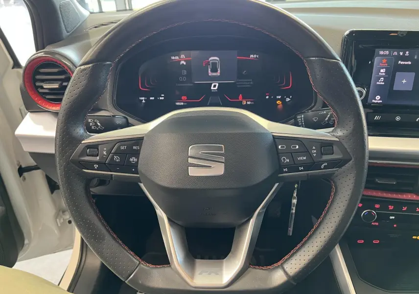 Vue frontale du volant sport cuir noir avec surpiqûres rouges du SEAT Arona blanc Nevada 2024, tableau de bord digital visible.