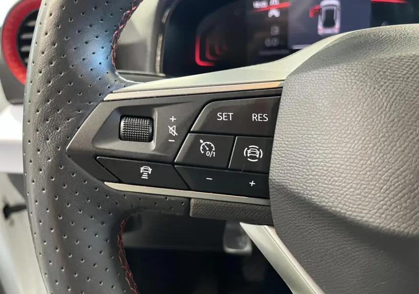 Gros plan sur le volant cuir perforé côté gauche du SEAT Arona blanc Nevada 2024 avec commandes de régulateur et aide à la conduite.