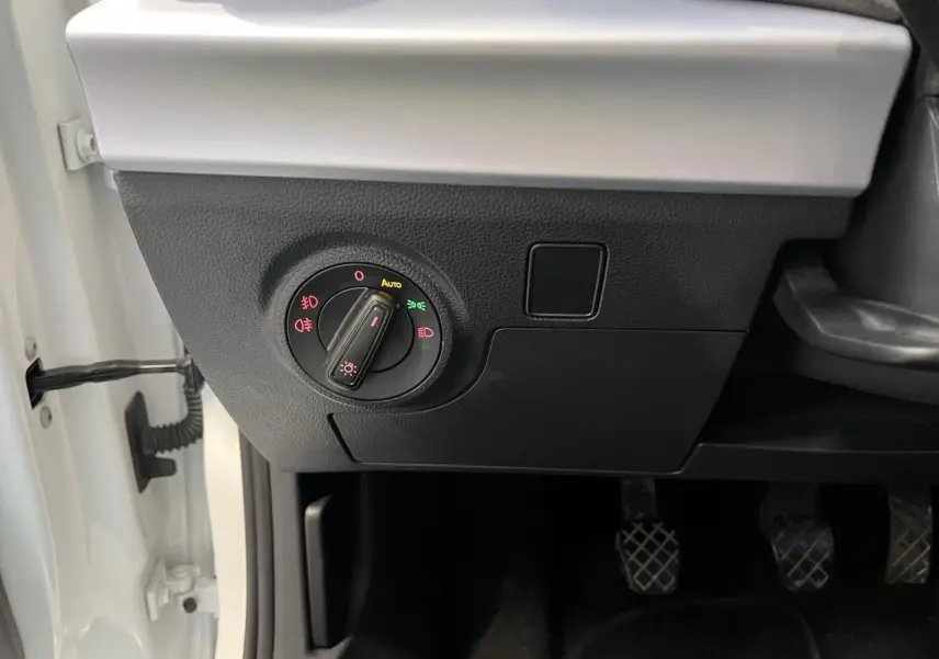 Gros plan sur le tableau de bord côté gauche d'une SEAT Arona blanc Nevada, montrant la commande des phares et les pédales.