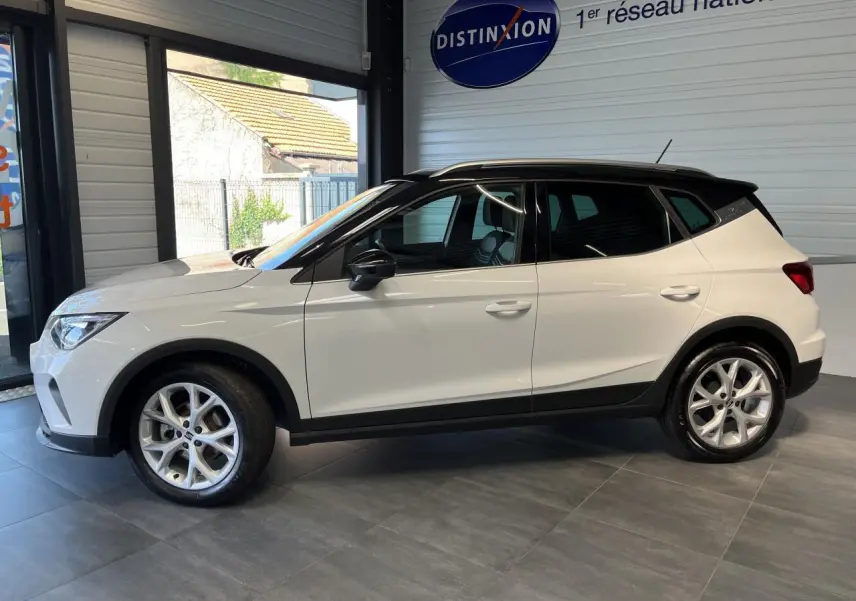 SEAT Arona blanc Nevada vu de profil côté gauche, avec toit noir et jantes alliage 16 pouces en showroom.