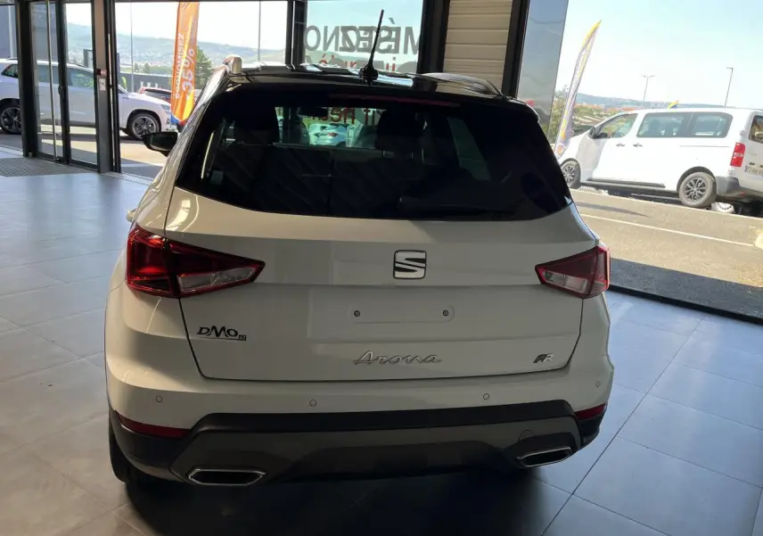 Vue arrière d'un SEAT Arona blanc Nevada 2024 avec logos et feux arrière anguleux en concession.