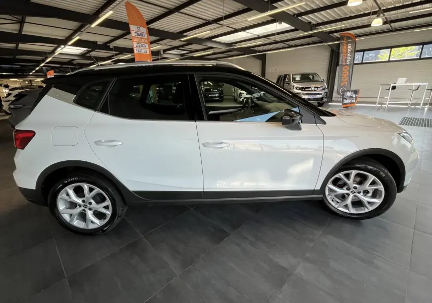 SEAT Arona blanc Nevada vue de profil côté gauche en intérieur, avec toit noir et jantes alliage 16 pouces.