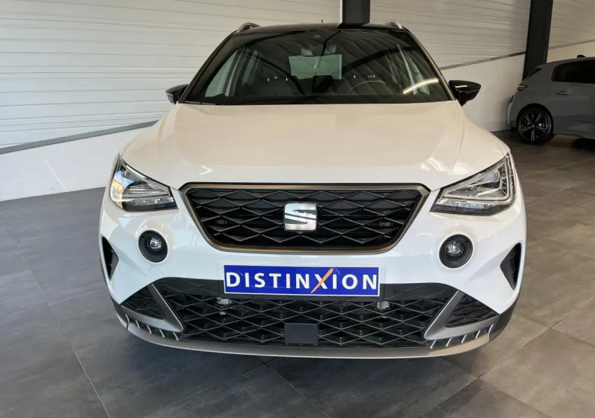 Vue frontale d'un SEAT Arona blanc Nevada avec calandre noire et logo central dans un showroom.