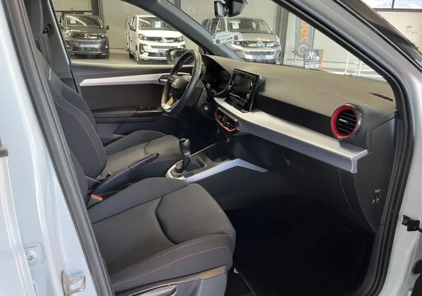 Intérieur côté conducteur du SEAT Arona blanc Nevada 2024, avec sellerie textile noire et volant sport cuir multifonction.